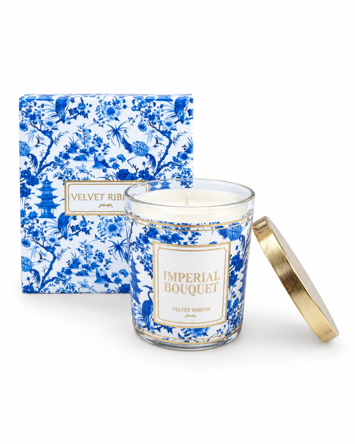 A luxury scented candle in a clear glass jar with a blue and white floral pattern, gold trim, and a gold lid resting beside it. The matching blue and white patterned box is positioned behind the candle on a clean white background.